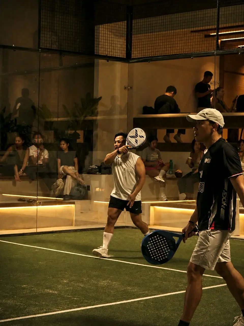 Evening match on the indoor court at Pad Thai Padel Canggu with spectators on the terrace