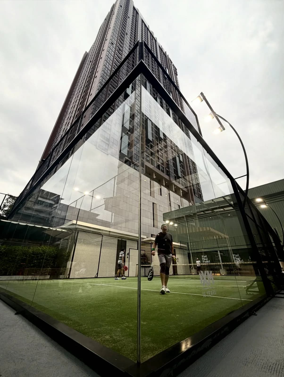 Glass padel court at Pad Thai Padel Rama 4 with a Bangkok tower rising behind it